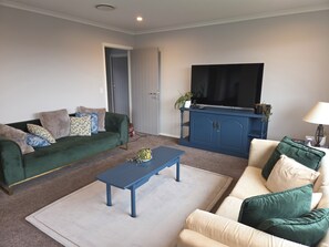 A living room with a green sofa, a blue coffee table, a beige sofa, a blue entertainment unit, and a TV. - Cosy and modern holiday retreat in beautiful Taupō (Taupō)