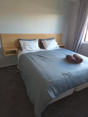 A neatly made bed with a headboard, pillows, and a pair of rolled towels. - Cosy and modern holiday retreat in beautiful Taupō (Taupō)