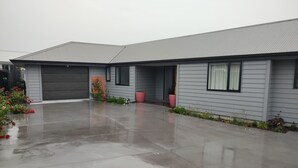Un edificio residenziale a due piani con garage, vialetto coperto e un piccolo giardino fiorito.