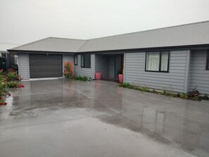 A two-story residential building with a garage, a covered driveway, and a small garden area with flowers and plants. - Cosy and modern holiday retreat in beautiful Taupō (Taupō)