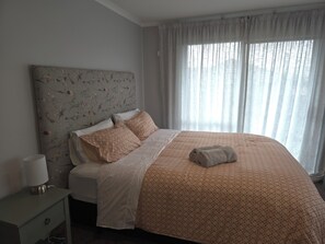 A hotel room with a bed, a nightstand, a lamp, and a window with curtains. - Cosy and modern holiday retreat in beautiful Taupō (Taupō)