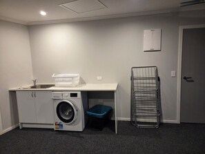 A laundry area with a washing machine, a sink, a drying rack, and a blue bin. - Cosy and modern holiday retreat in beautiful Taupō (Taupō)