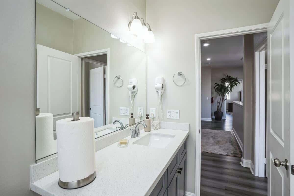 Une salle de bain avec un grand miroir, deux lavabos, un porte-rouleau de papier toilette et un porte-serviette.