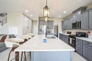Una cocina moderna con gabinetes grises, una isla central, un refrigerador de acero inoxidable y un microondas.