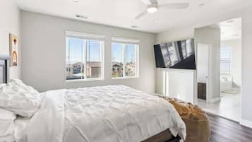 A bedroom with a bed, a ceiling fan, a TV, and a view of the outside.