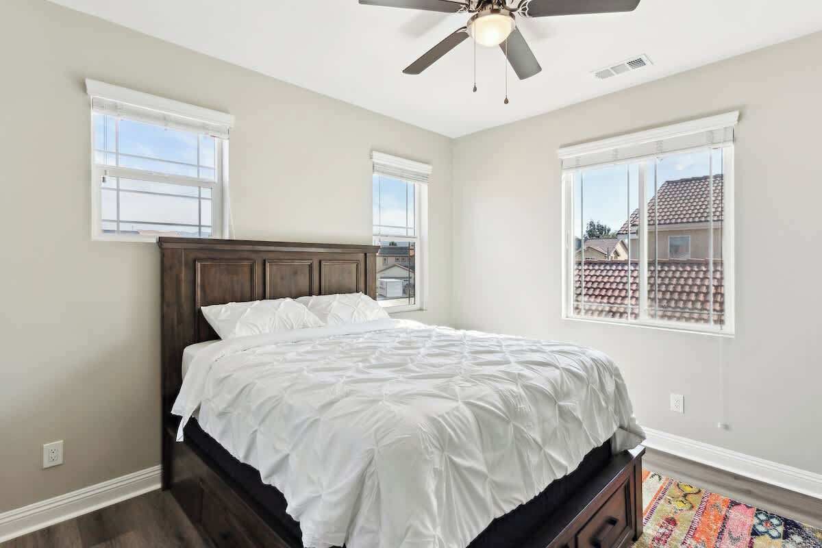 A bedroom with a bed, a ceiling fan, and two windows.