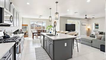 A modern kitchen with a central island, dining area, and a living space with a sofa and TV.