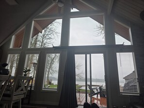 A room with large windows, a view of a lake, and a deck area with outdoor furniture.