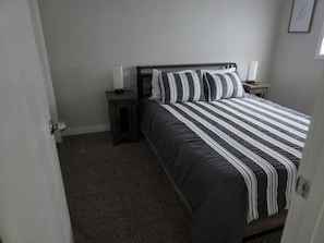 A bedroom with a bed, a nightstand, a lamp, and a door.