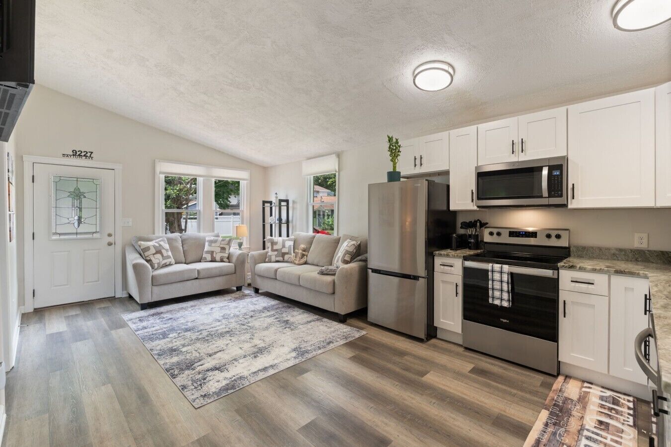 A modern kitchen with white cabinets, stainless steel appliances, and a grey patterned rug.