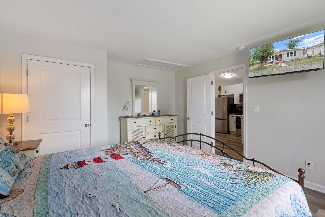 Ein Schlafzimmer mit Bett, Kommode, Spiegel und einem Fernseher, der ein Haus zeigt.