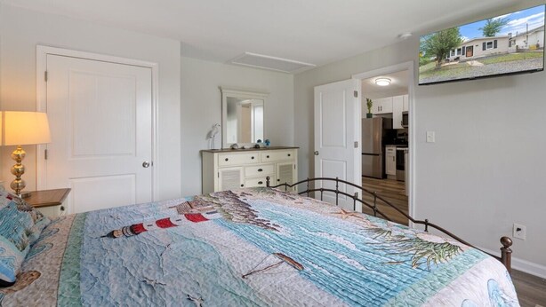 Een slaapkamer met een bed, dressoir, spiegel en een televisie waarop een huis te zien is.