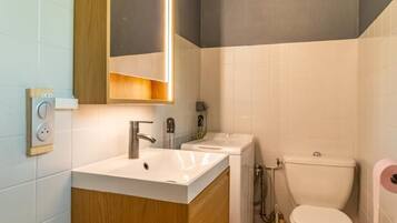 Un baño moderno con tocador de madera, un espejo grande, un lavamanos blanco, un inodoro y un pequeño cubo de basura.