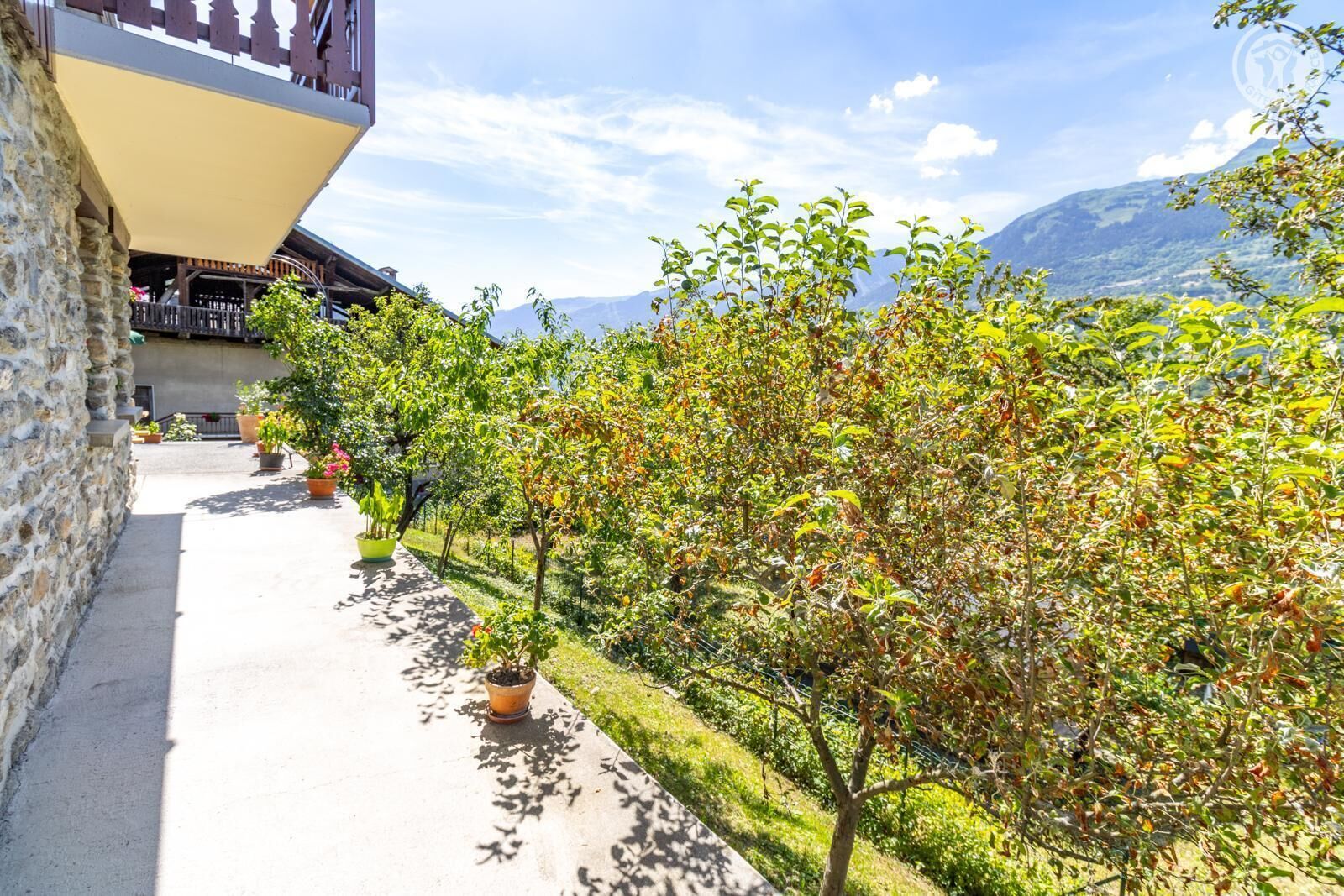 Un bâtiment en pierre doté d’un balcon, de plantes en pot et offrant une vue sur les montagnes.