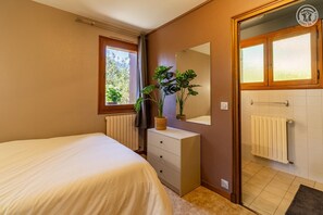 Un dormitorio con cama, cómoda, espejo, radiador y ventana con cortinas.