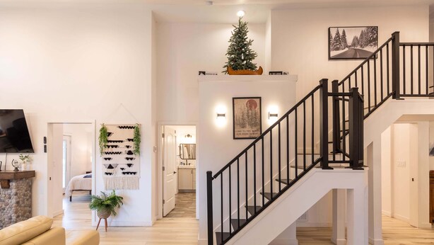 Ein modernes Interieur mit Treppe, einem Wohnbereich inklusive Sofa und Fernseher sowie einem Flur, der in einen weiteren Raum führt.