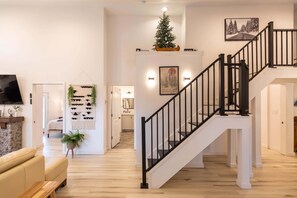 A modern interior with a staircase, a living area with a sofa and a TV, and a hallway leading to another room. - Mill Timber Lodge: Creekfront home, dog friendly, firepit, yard, deck, WiFi & grill! (Newland)