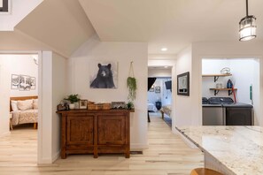 A modern interior with a wooden cabinet, a bear painting, and a kitchen area with appliances. - Mill Timber Lodge: Creekfront home, dog friendly, firepit, yard, deck, WiFi & grill! (Newland)