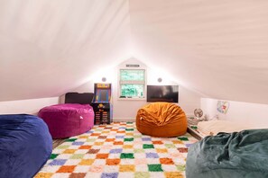 A cozy attic room with a checkered floor, bean bags, a retro video game console, and a large TV. - Mill Timber Lodge: Creekfront home, dog friendly, firepit, yard, deck, WiFi & grill! (Newland)