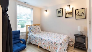 Ein Schlafzimmer mit einem Einzelbett, einem blauen Sessel, einem kleinen Tisch mit Lampe und drei gerahmten Bildern an der Wand.