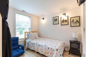 Ein Schlafzimmer mit einem Einzelbett, einem blauen Sessel, einem kleinen Tisch mit Lampe und drei gerahmten Bildern an der Wand.