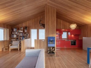 Ein großzügiges Loft mit hohen Decken, Holzwänden, einer integrierten Bücherreol und einer gemütlichen Sitzecke, sowie einer modernen Küche mit roten Küchenschränken.