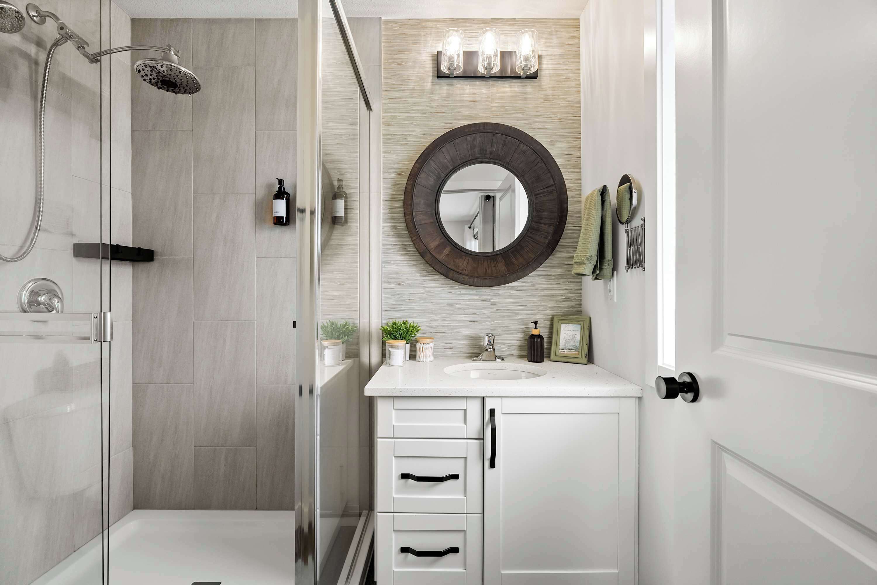 A modern bathroom with a glass shower enclosure, a round mirror, and a white vanity with a sink.