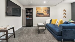 A living room with a flat-screen TV, a bookshelf, a painting, a sofa, and a coffee table. - On The Ridge | Sleeps 8 | A/C | Gym Equipment | (Sylvan Lake)