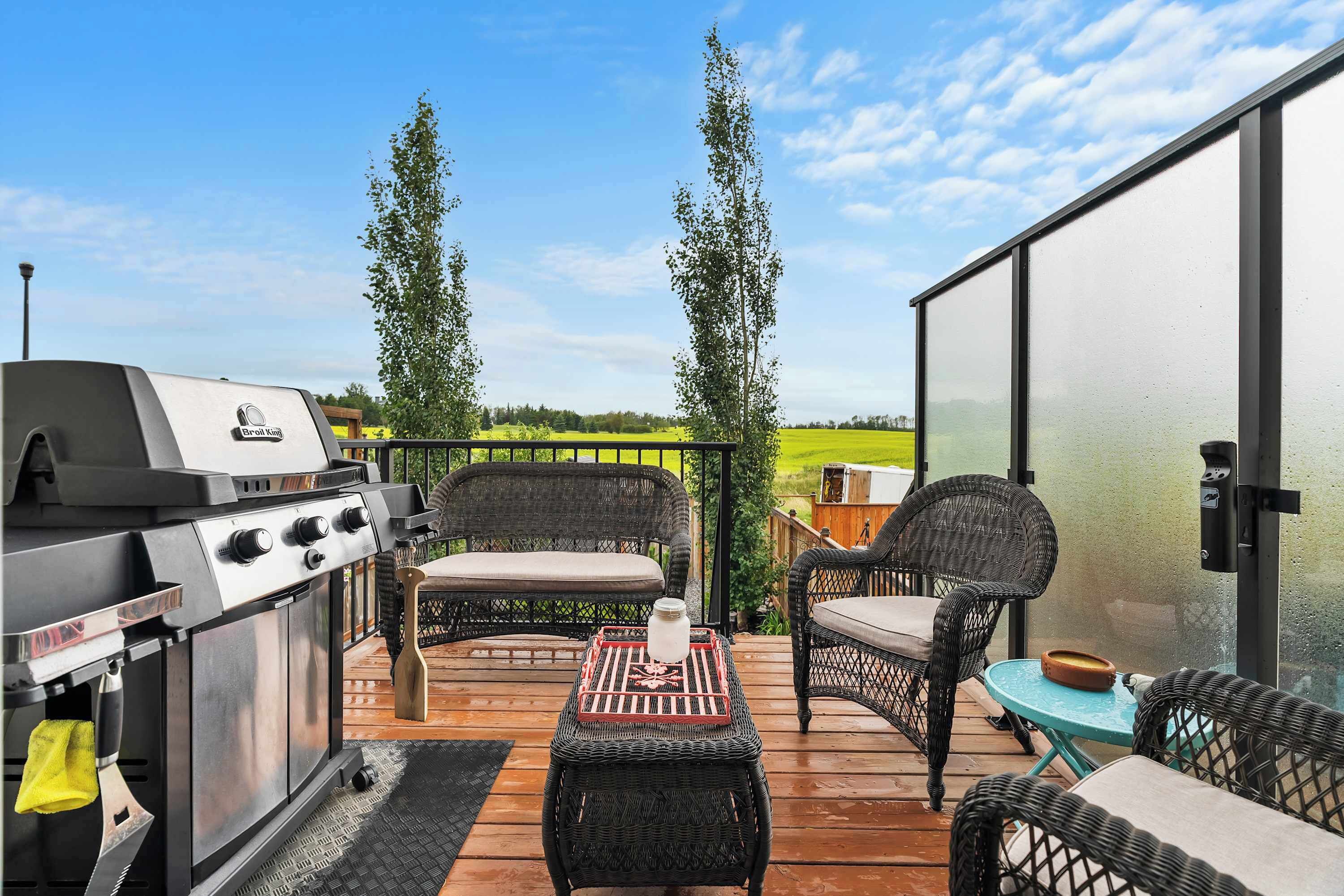 An outdoor patio with a grill, wicker furniture, and a view of the countryside.