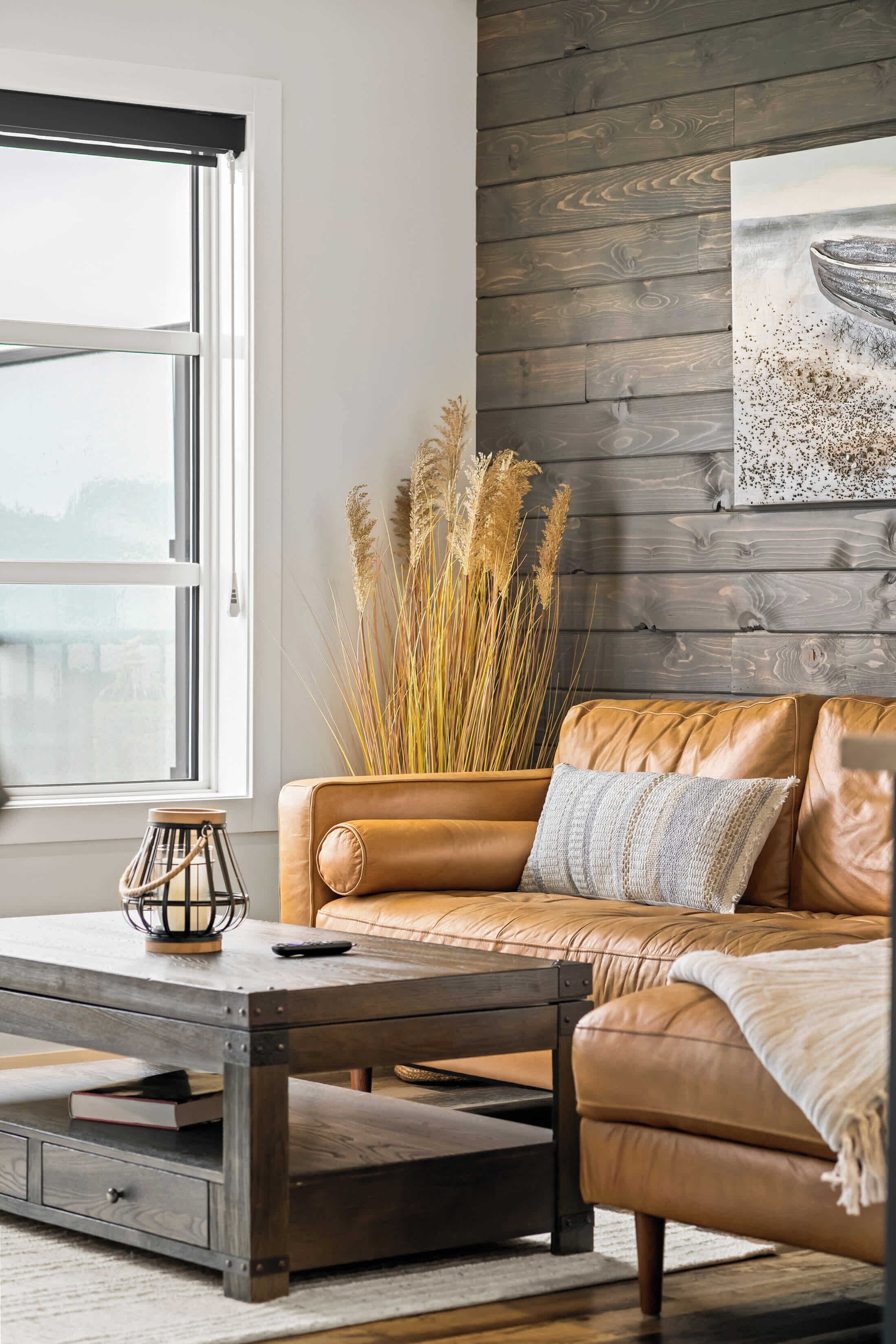 A modern living room with a leather sofa, a coffee table, and a decorative vase with tall grasses.