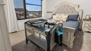 Une chambre à coucher avec un lit, un berceau, une fenêtre donnant sur un beau paysage et une table de chevet.
