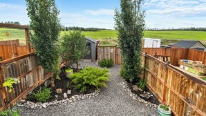 Une cour arrière clôturée avec un chemin de gravier, un petit abri de jardin et une clôture en bois.