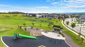 Une aire de jeux avec des toboggans et des structures d’escalade, entourée d’un espace vert et bordée, au loin, par des immeubles d’habitation.