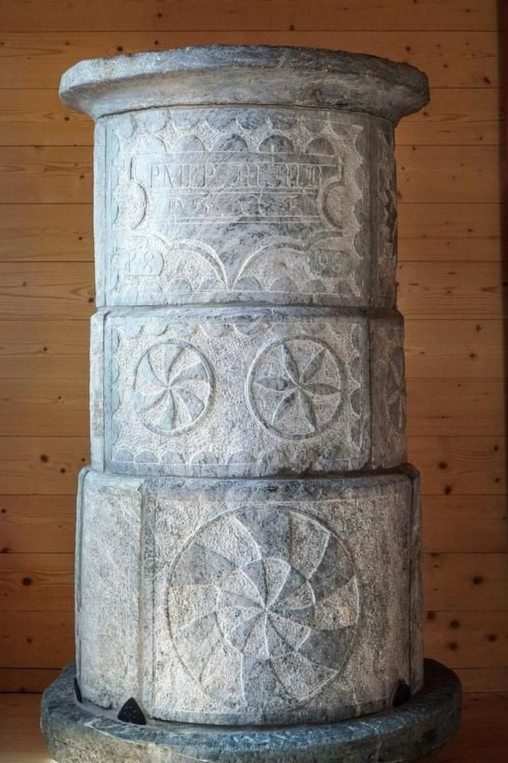 A stone pillar with carved symbols and text, set against a wooden background.