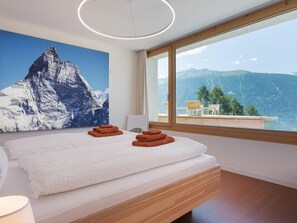 Ein Schlafzimmer mit einem großen Bett, Bergblick und einer modernen Deckenleuchte.