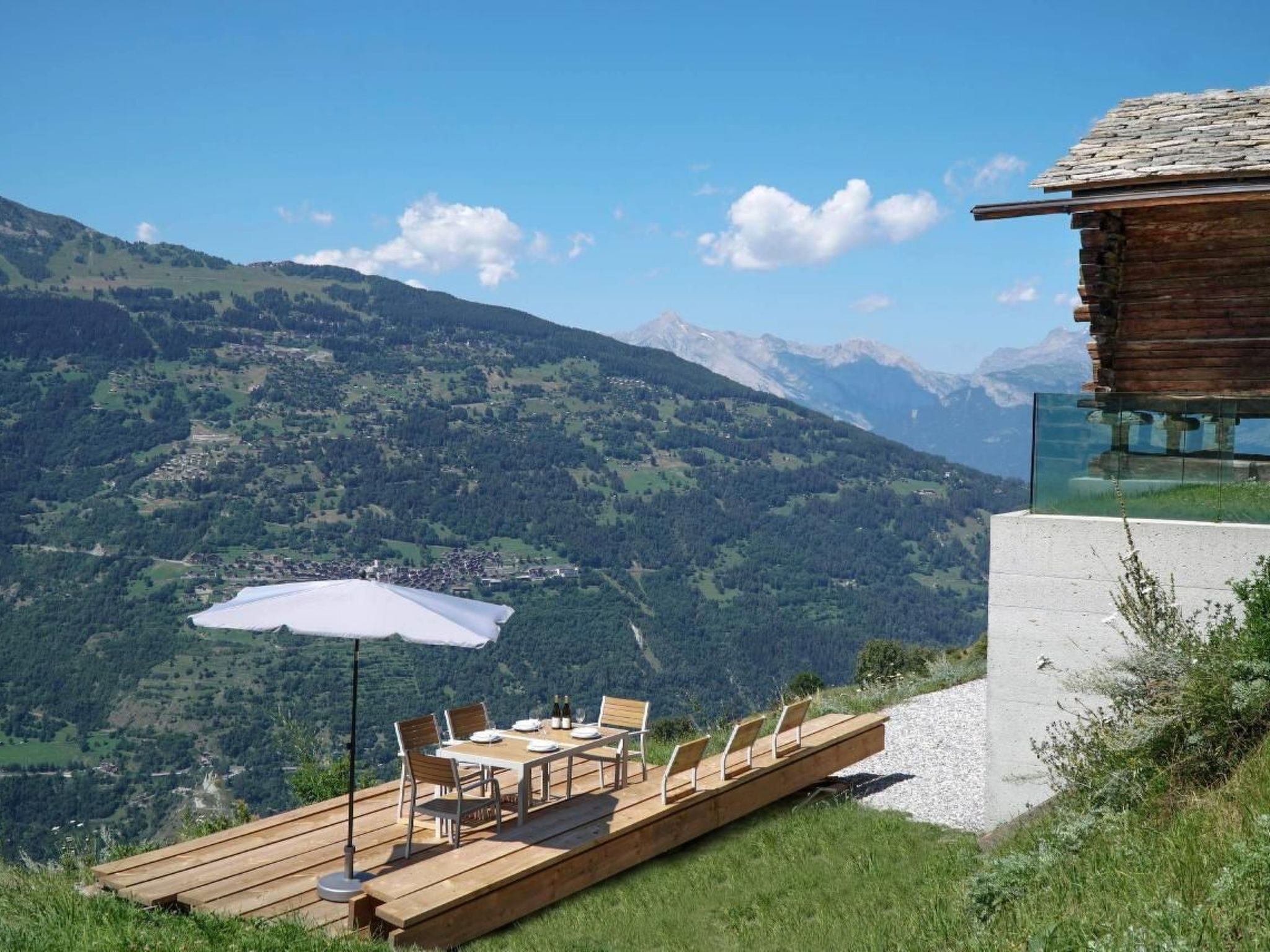 Une terrasse en bois avec une table et des chaises, offrant une vue sur un paysage montagneux.