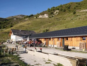Un edificio rústico con techo inclinado, mesas al aire libre y un pequeño arroyo en primer plano.
