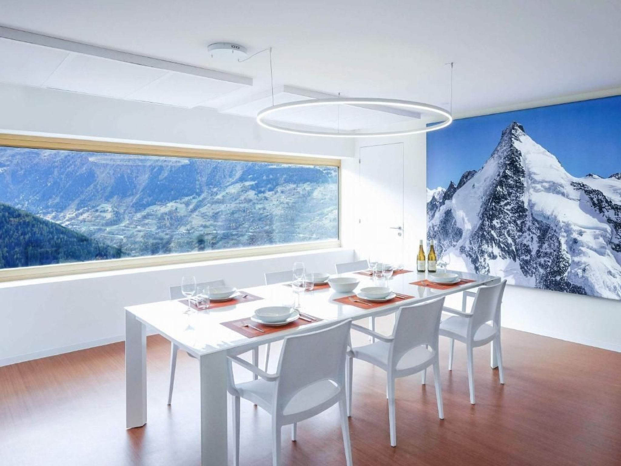 Une salle à manger moderne avec une grande fenêtre, des meubles blancs et une vue sur les montagnes.