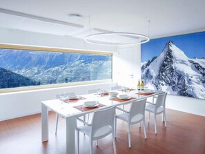 A modern dining room with a large window, white furniture, and a mountain view. - Exklusives Architektur-Chalet in toller Lage by Interhome (St-Martin VS)