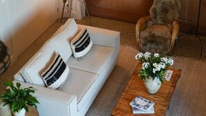 En hyggelig stue med en hvid sofa, en lampe, et træsofabord med en plante, og en kat.