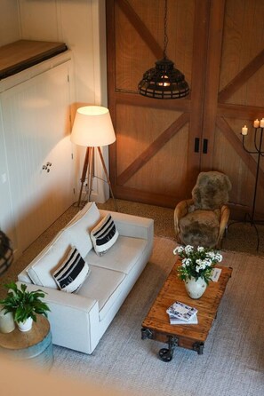 A cozy living room with a white sofa, a lamp, a wooden coffee table with a plant, and a cat. - The Boat House - Rustic Luxury in Matakana (Matakana)