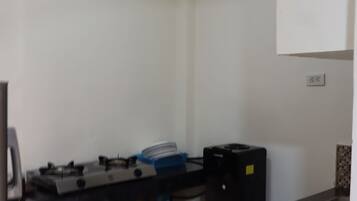 A small kitchen with a gas stove, a water dispenser, and a trash bin.