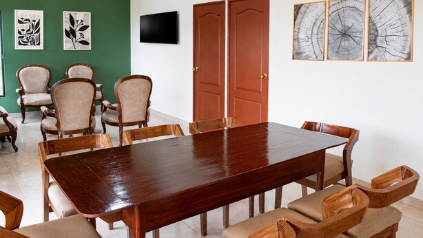 A conference room with a long wooden table, beige upholstered chairs, and a green accent wall.