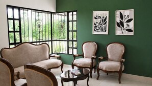 A room with a green wall, two framed black and white floral artworks, and four upholstered chairs with wooden frames.