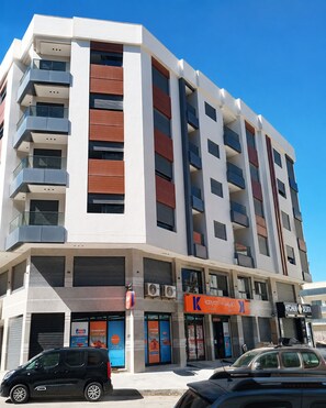 A multi-story building with balconies, a ground-level commercial space, and a parked car. - Modern 1BR Netflix • WiFi • Free Parking (Tangier)