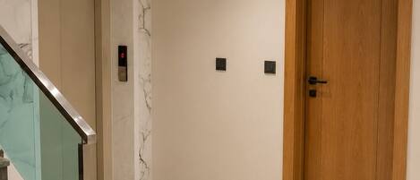 A hallway with a marble wall, a wooden door labeled '15', and a glass staircase.