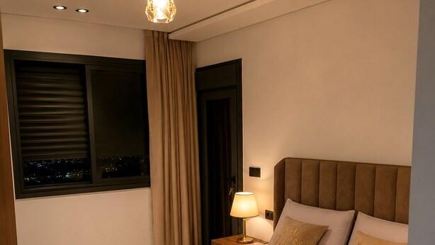 A modern bedroom with a large bed, a nightstand, a lamp, and a view of the city through the window. - Modern 1BR Netflix • WiFi • Free Parking (Tangier)