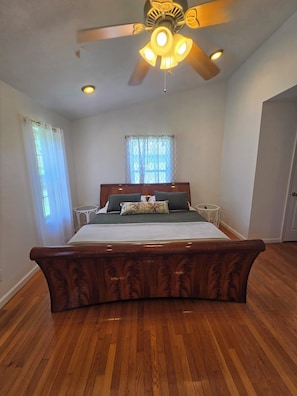 Un dormitorio con una cama de madera, ventilador de techo y una ventana con cortinas.