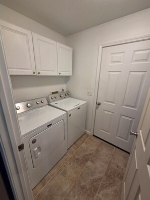 A laundry room with two washing machines, a dryer, and a white door.