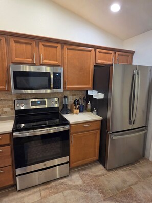 A kitchen with stainless steel appliances, wooden cabinets, and a tiled backsplash.